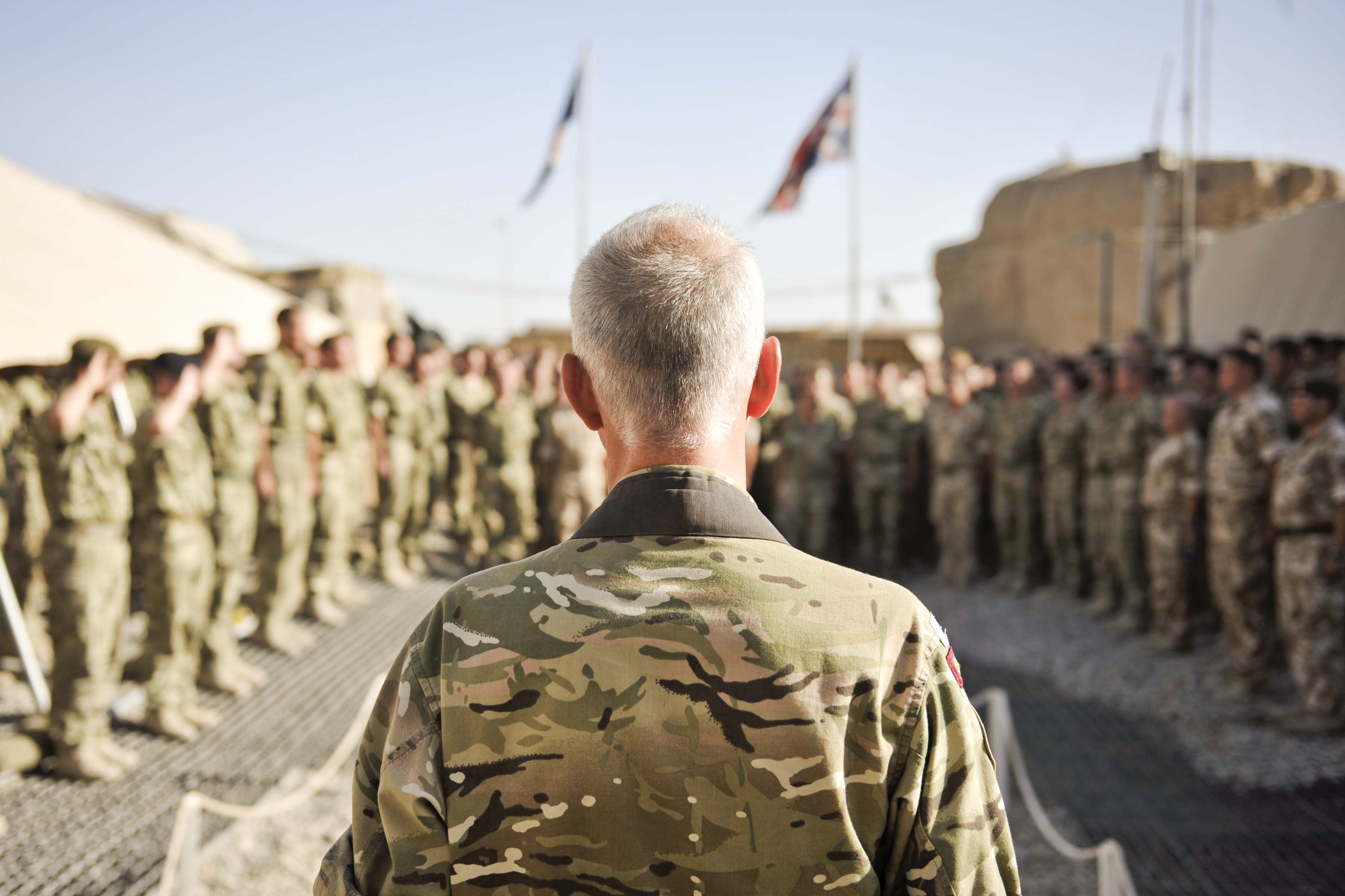 An Army chaplain standing with his back to camera leading worship for soldiers in a horseshoe formation standing in front of him