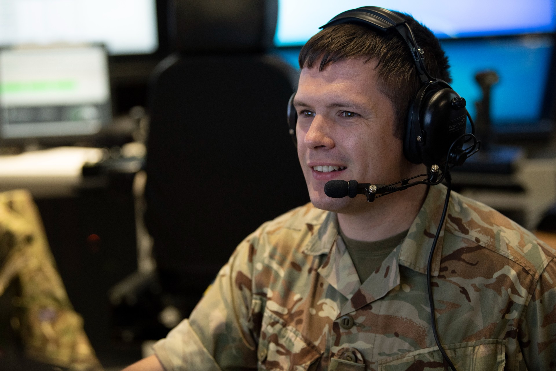 Man in Army uniform wearing a headset looking at a computer