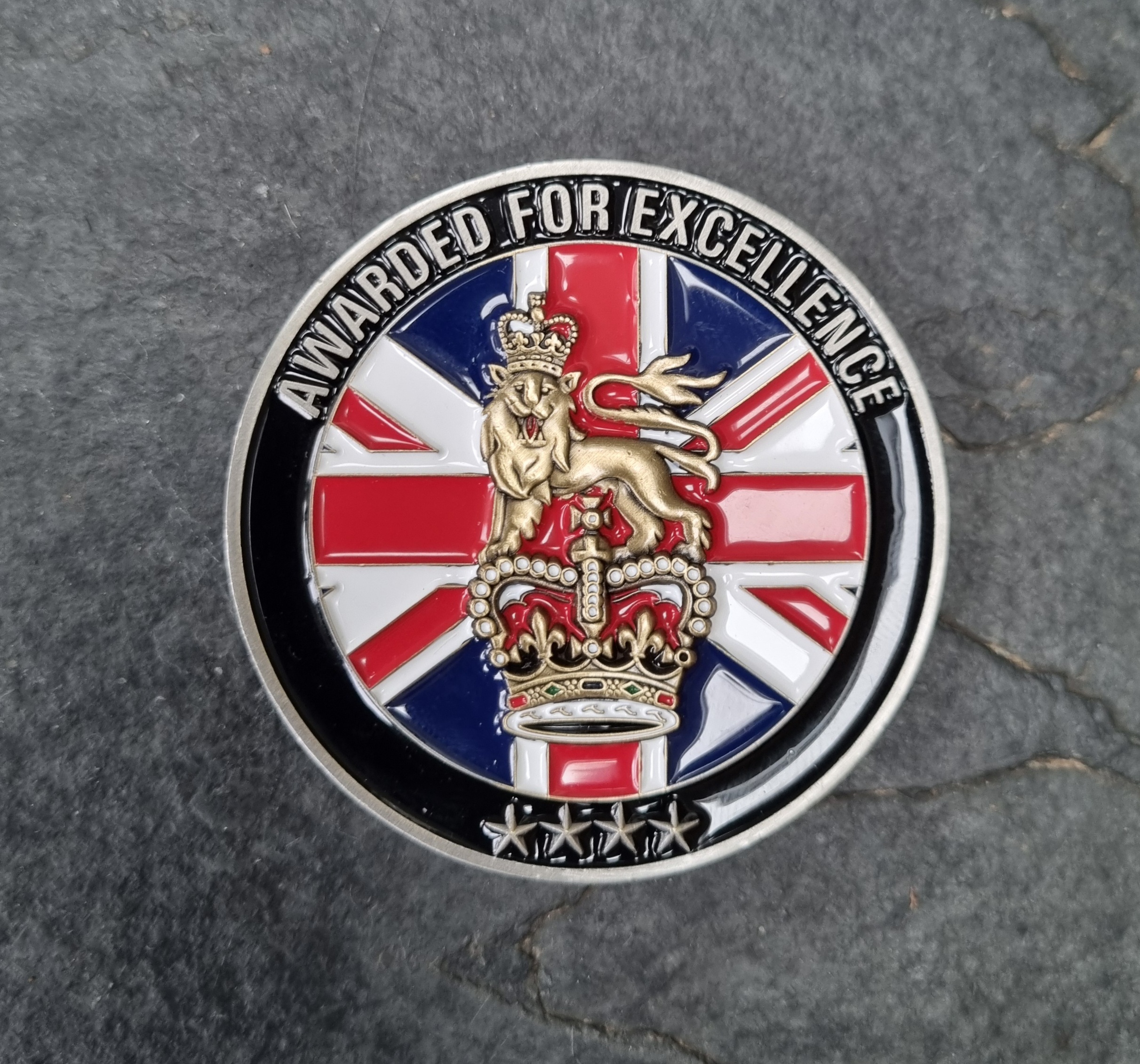 A coin with text 'awarded for excellent' on the edge and union jack flag with military crest.