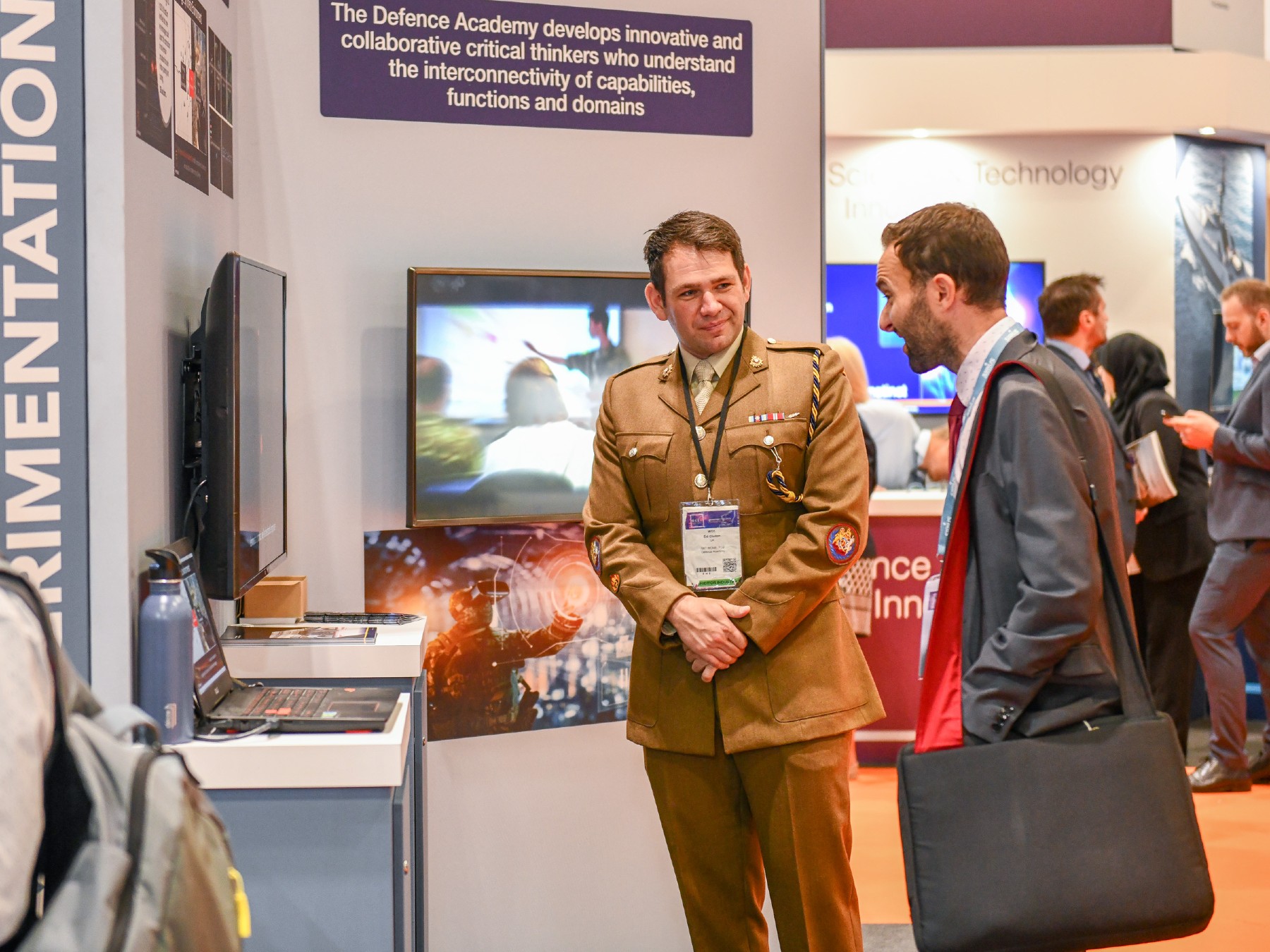 Man in Army uniform talking to another man in business attire at a conference exhibition