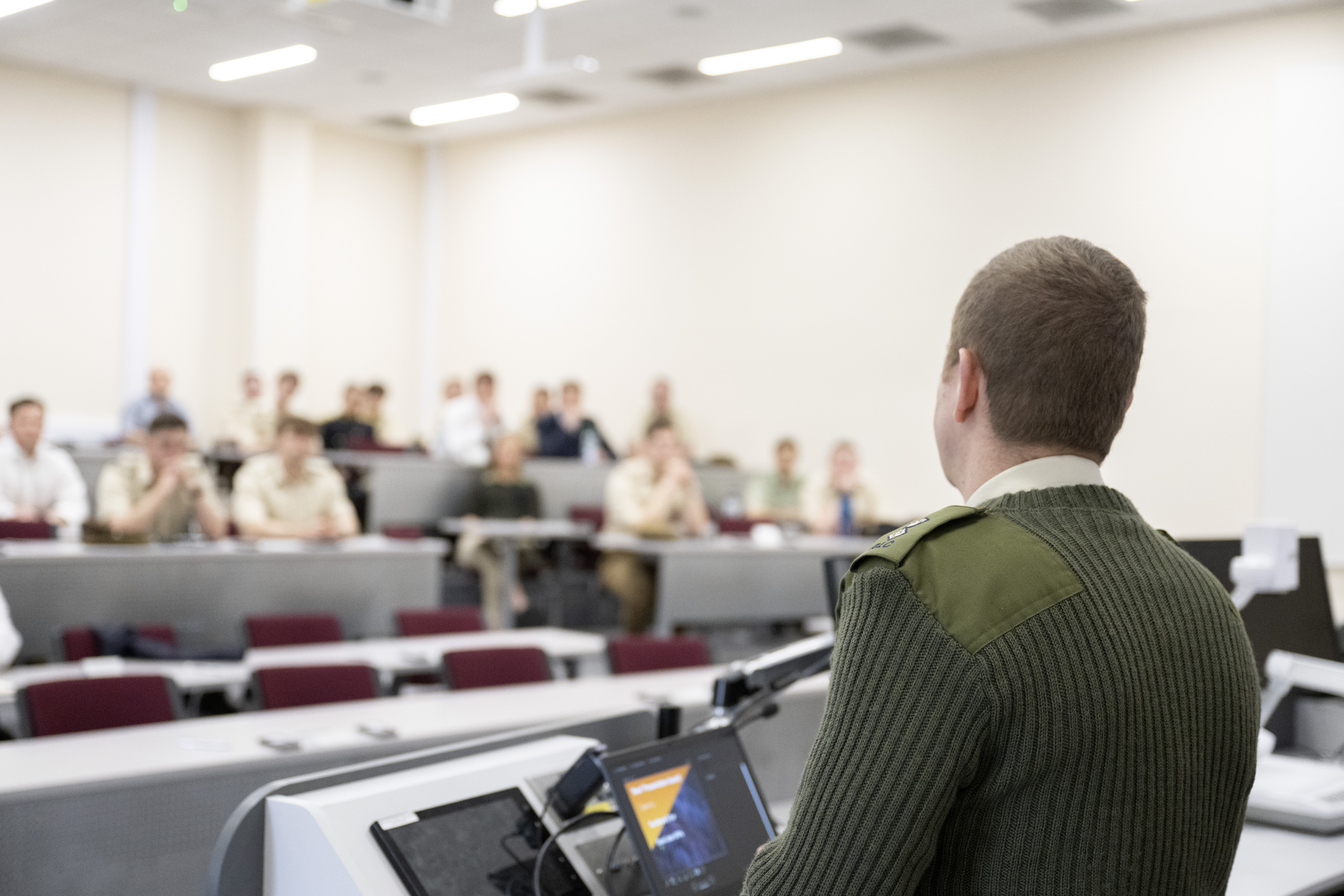 An army officer stood at a lectern presenting to an audience.