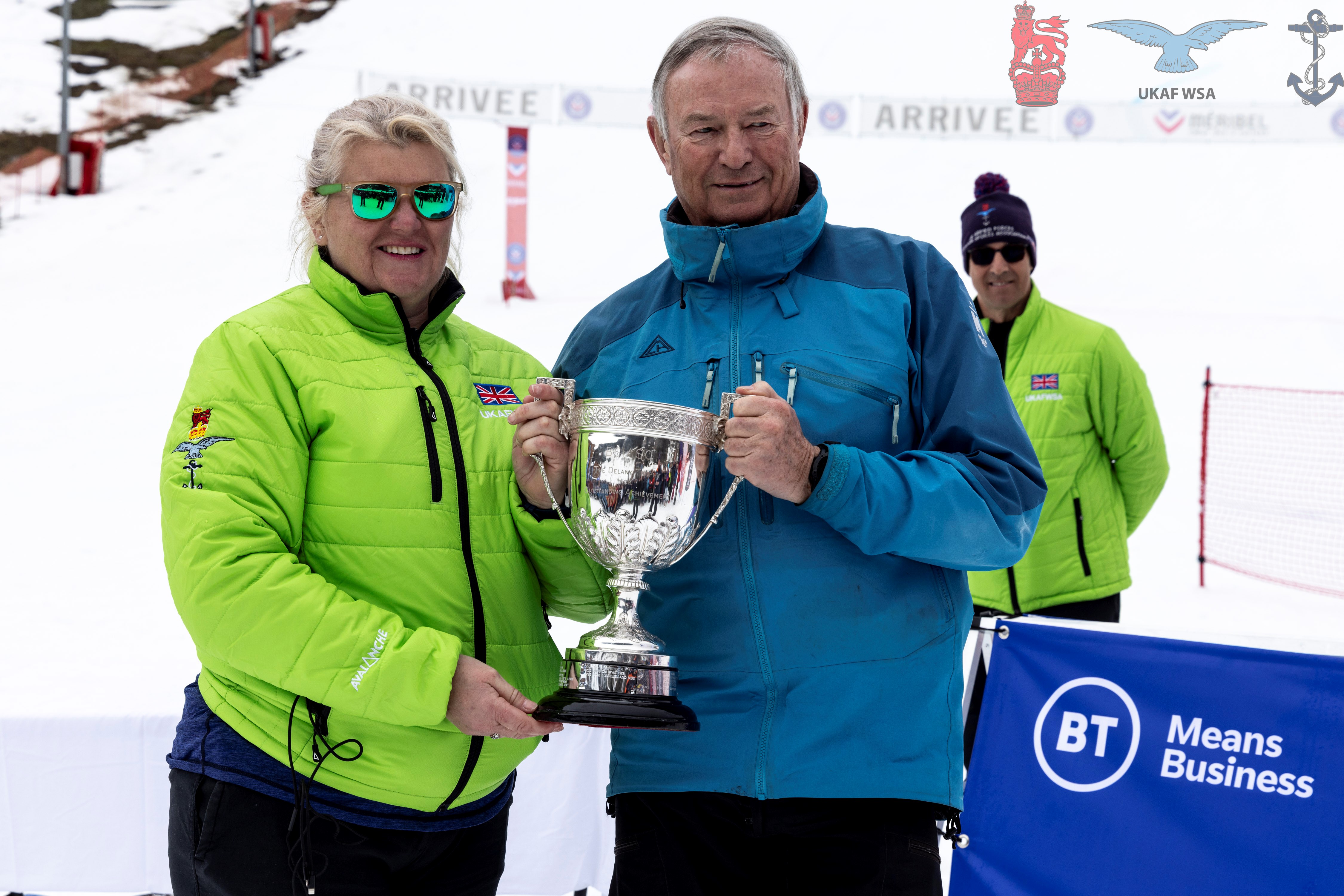 Cdr Nicky Cullen being presented with the Oliver Delaney Trophy in front of snowy ski slopes. 