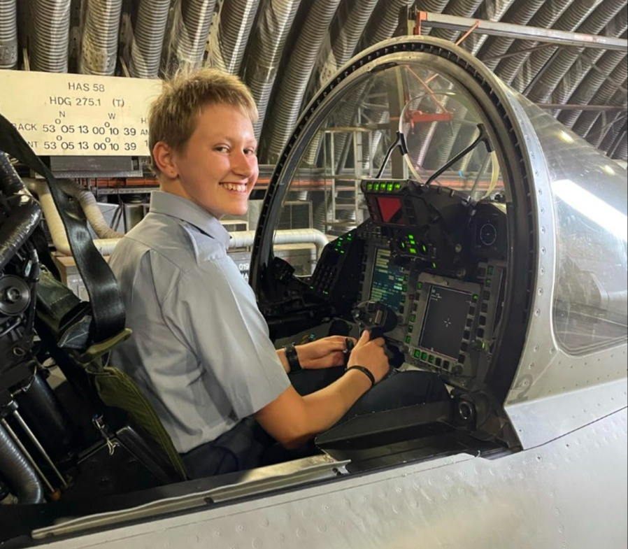 A female officer cadet seated in a cockpit smiling at the camera