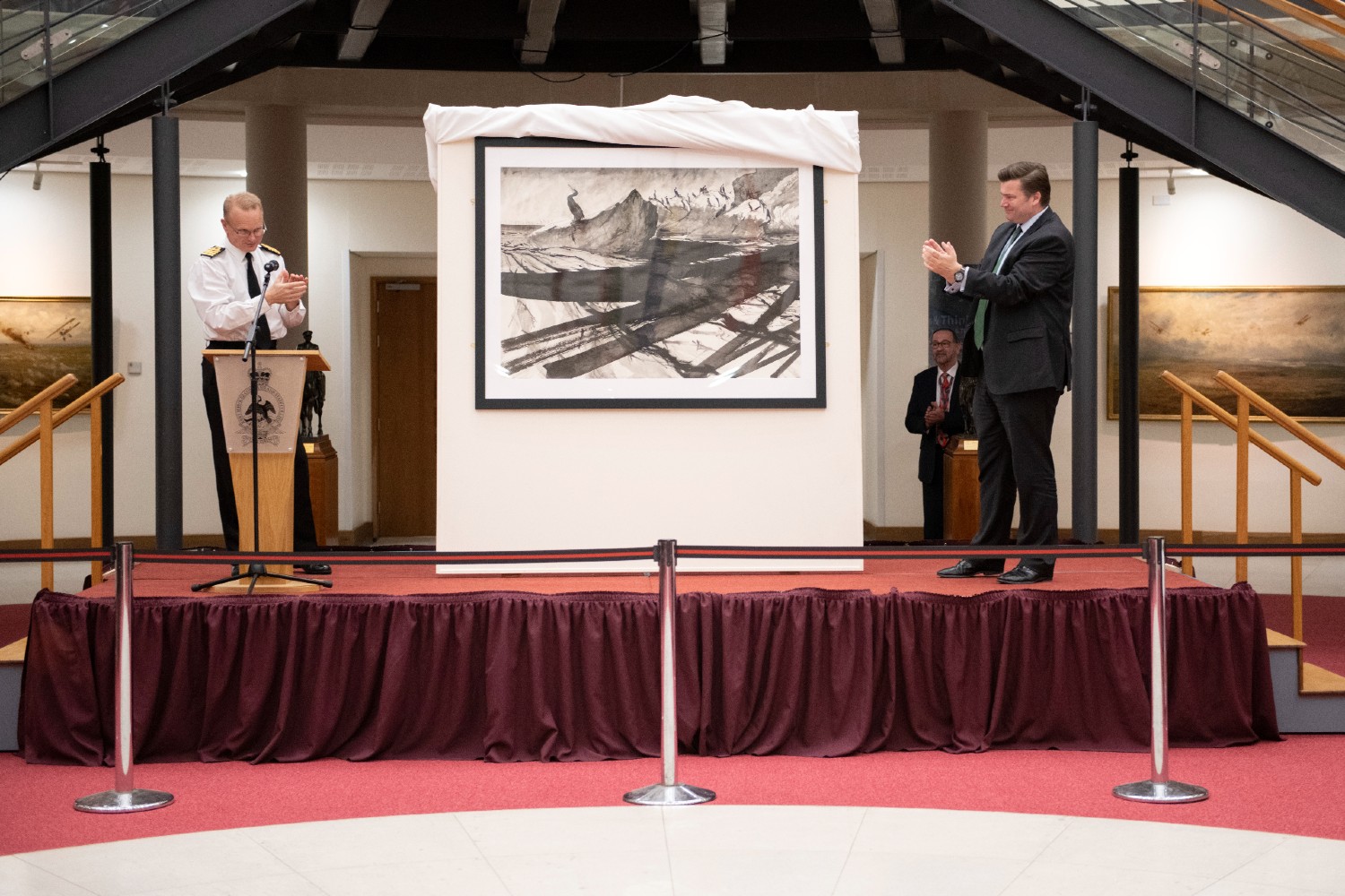 A navy officer and Minister for the Armed Forces unveiling an artwork depicting the Cormorant bird.