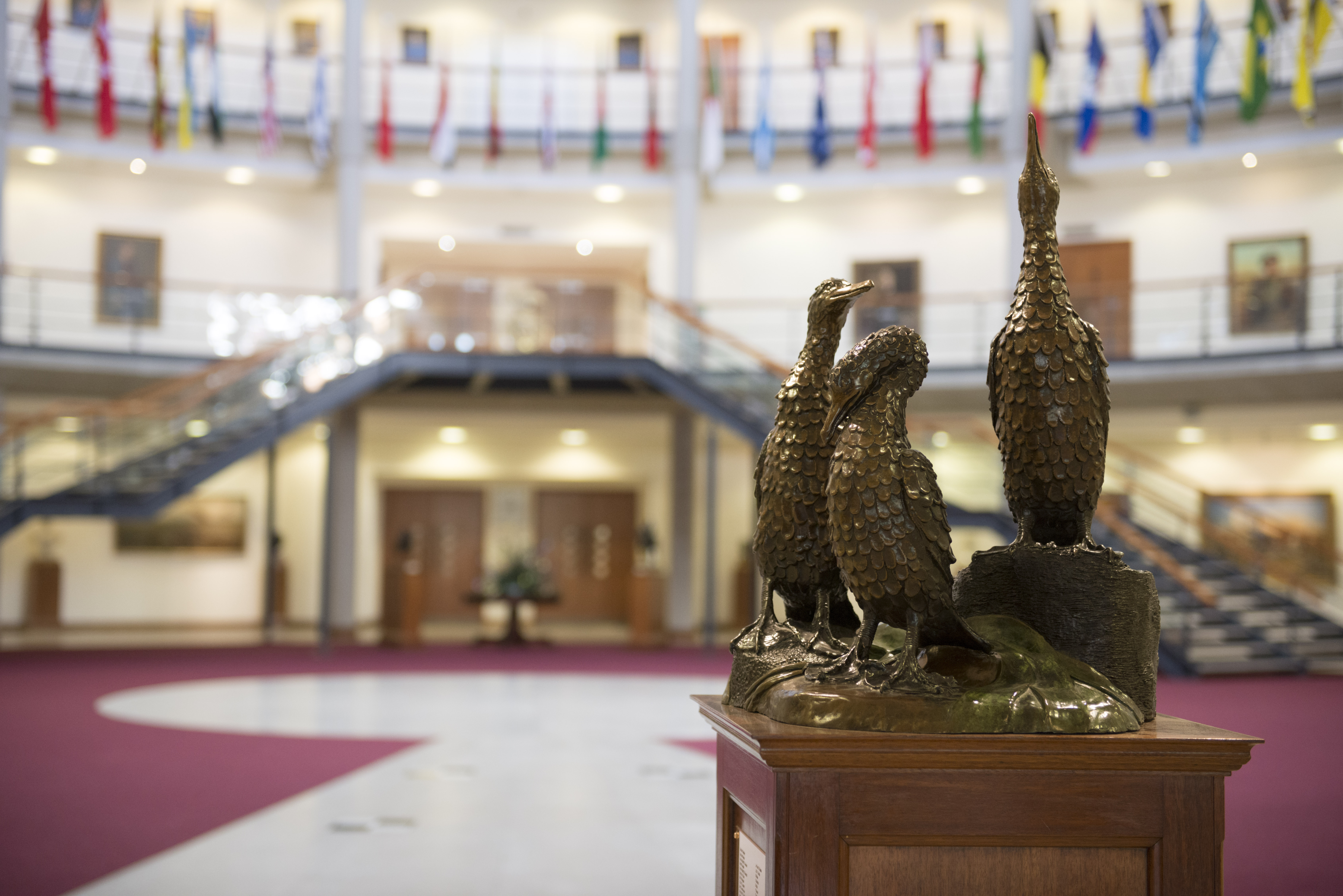 A gold statue of 3 cormorant birds inside a forum filled with multiple handing flags from around the world.