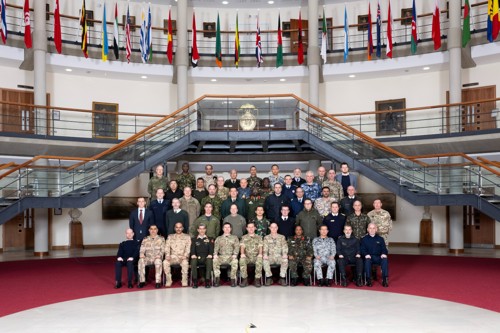 The whole International Defence Attache party in a group event photo in the forum surrounded by international flags above them.