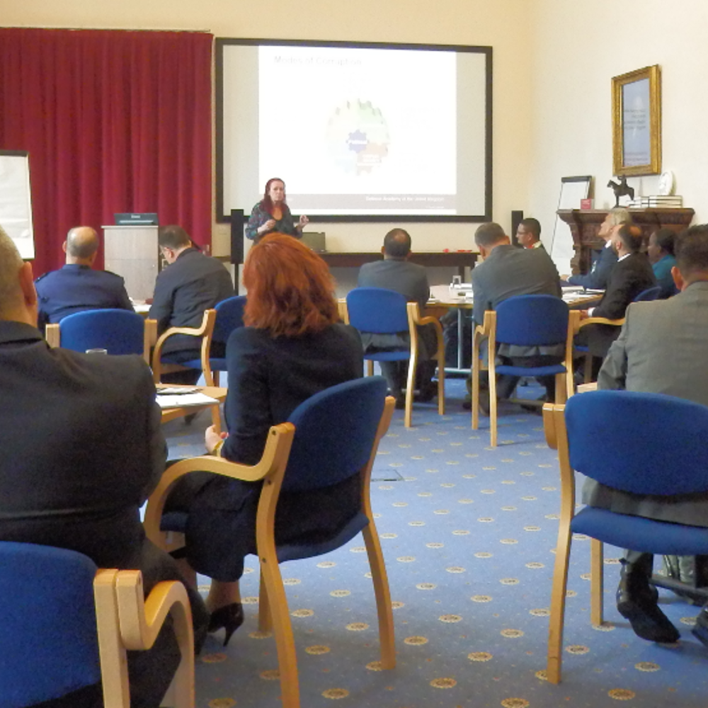 A group of people sat around tables in a syndicate room while being presented to.