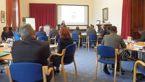 A group of people sat around tables in a syndicate room while being presented to.