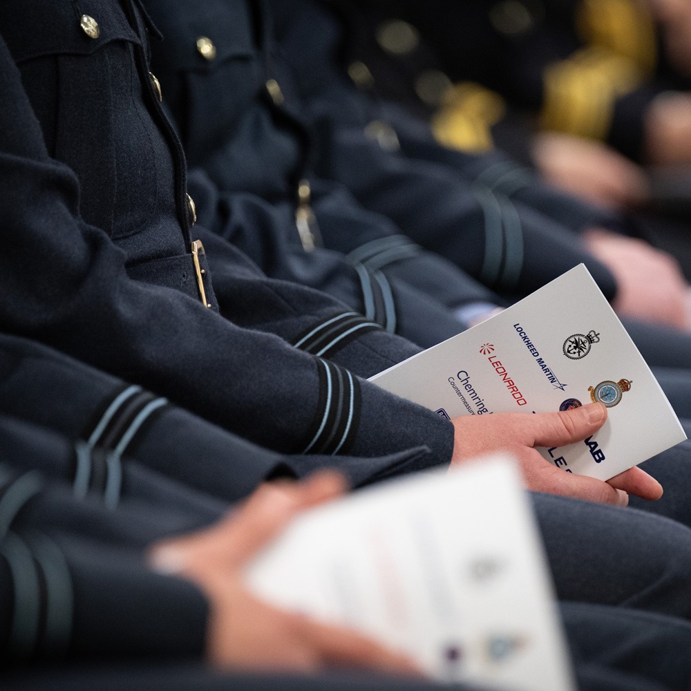 Close-up of uniformed individuals seated in a row holding official ceremony programs with insignias visible.