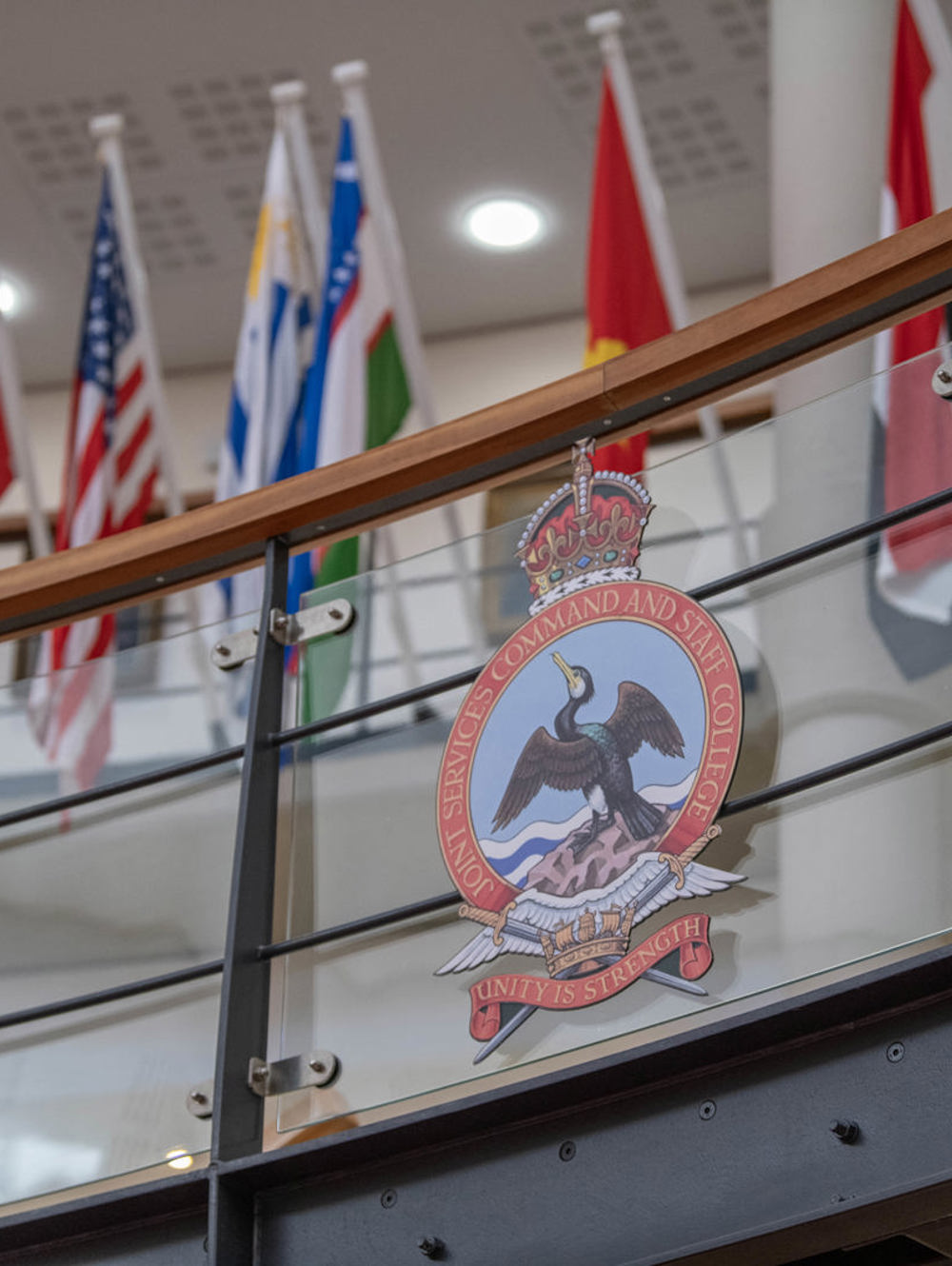A staircase balcony displaying the JSCSC crest flanked by rows of international flags.