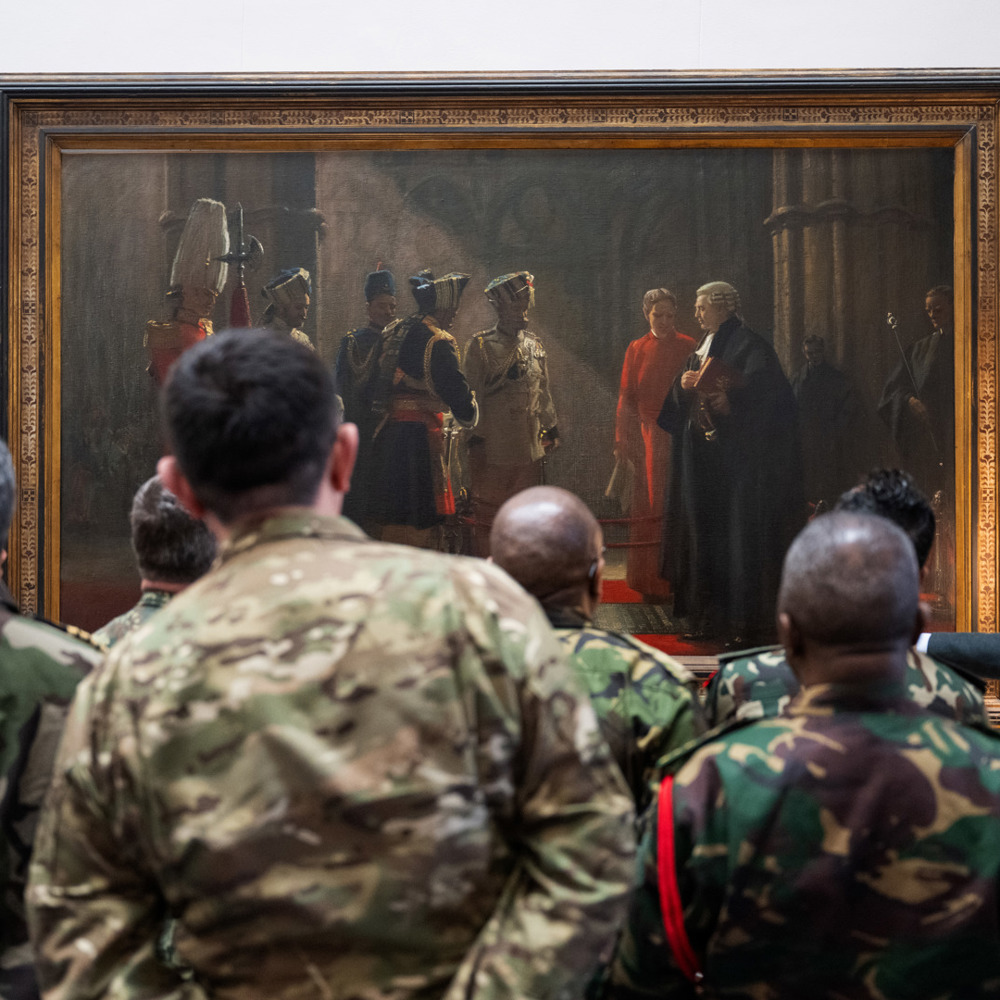 Group of military personnel in various camouflage uniforms observing a large historical painting in a gallery setting.