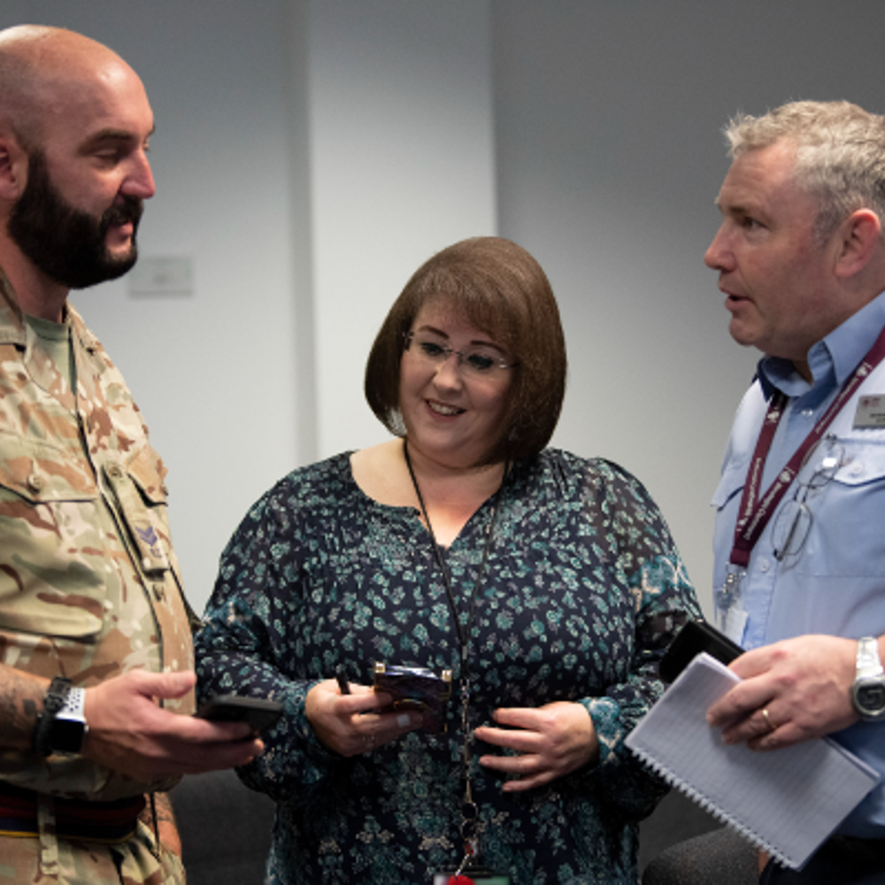 Three people standing in a group talking, one in Army uniform, others in business attire