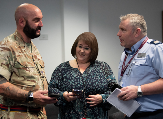 Three people standing in a group talking, one in Army uniform, others in business attire