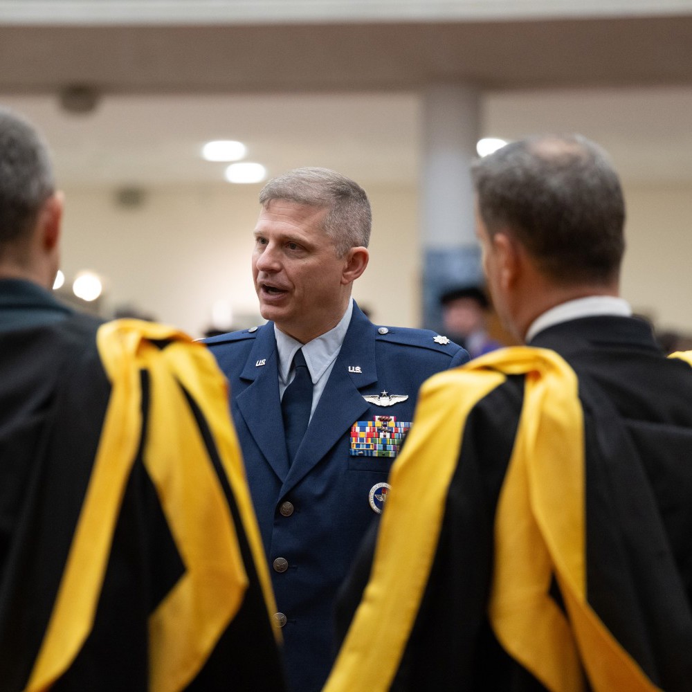 US RAF officer talking to graduates showing the backs of their black and yellow gowns.
