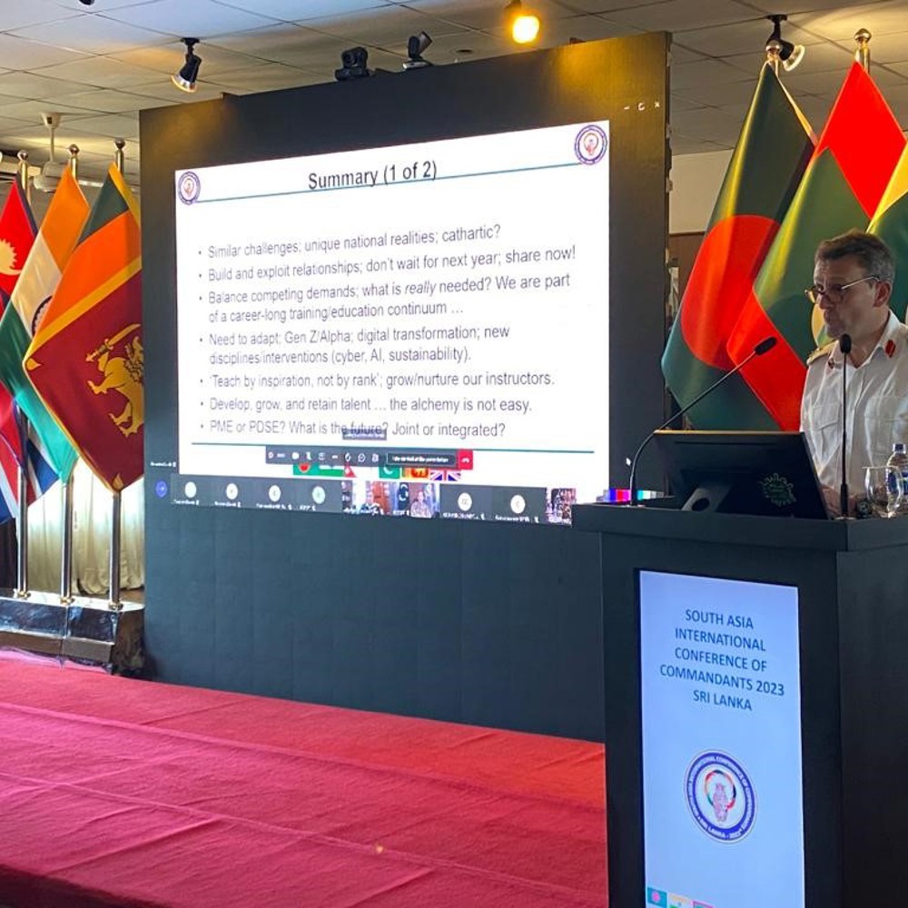 Major General Roe giving a presentation surrounded by international flags.