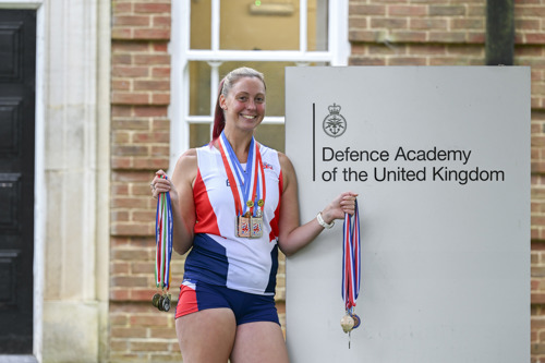 A woman stood beside a Defence Academy of the UK sign holding up her European Athletics medals. 