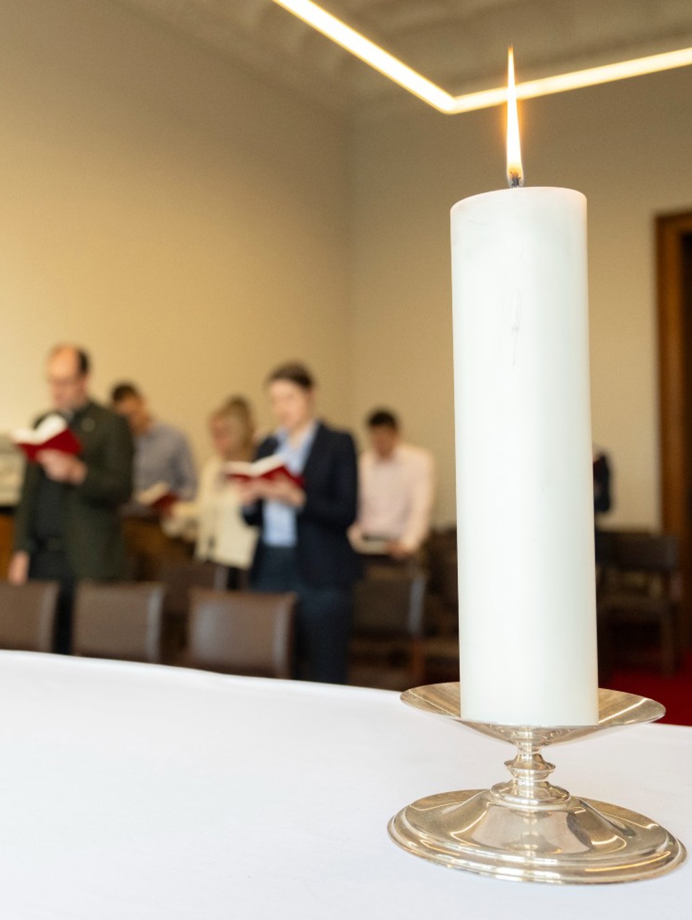 Chapel alter with tall candle and crucifix, with congregation behind.