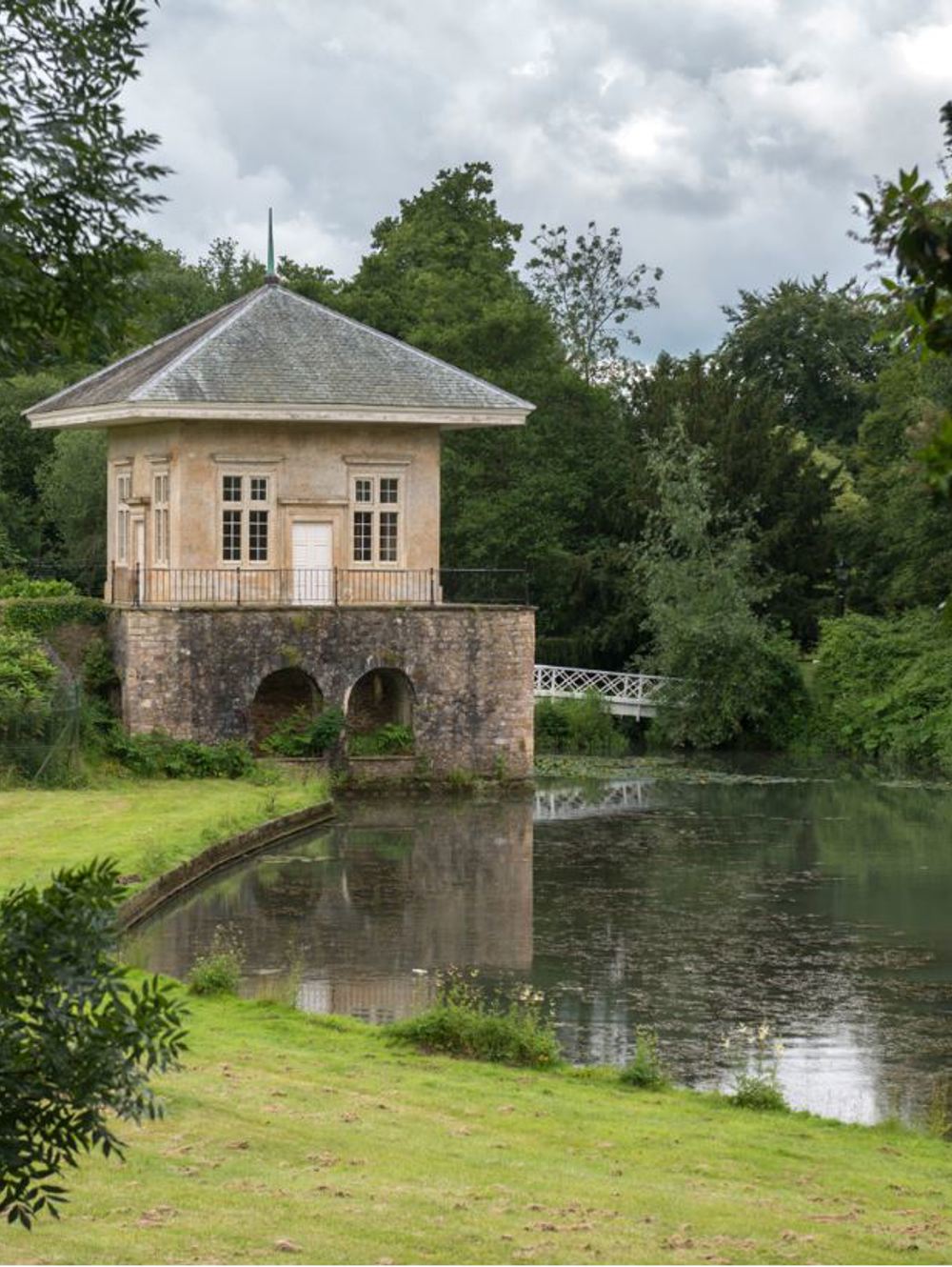 A small building situated over a lake with greenery surrounding it.