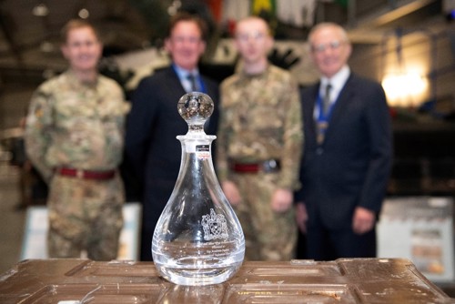 A cut glass decanter resting on a trunk in the foreground while the winner and presenters are in the background, blurred