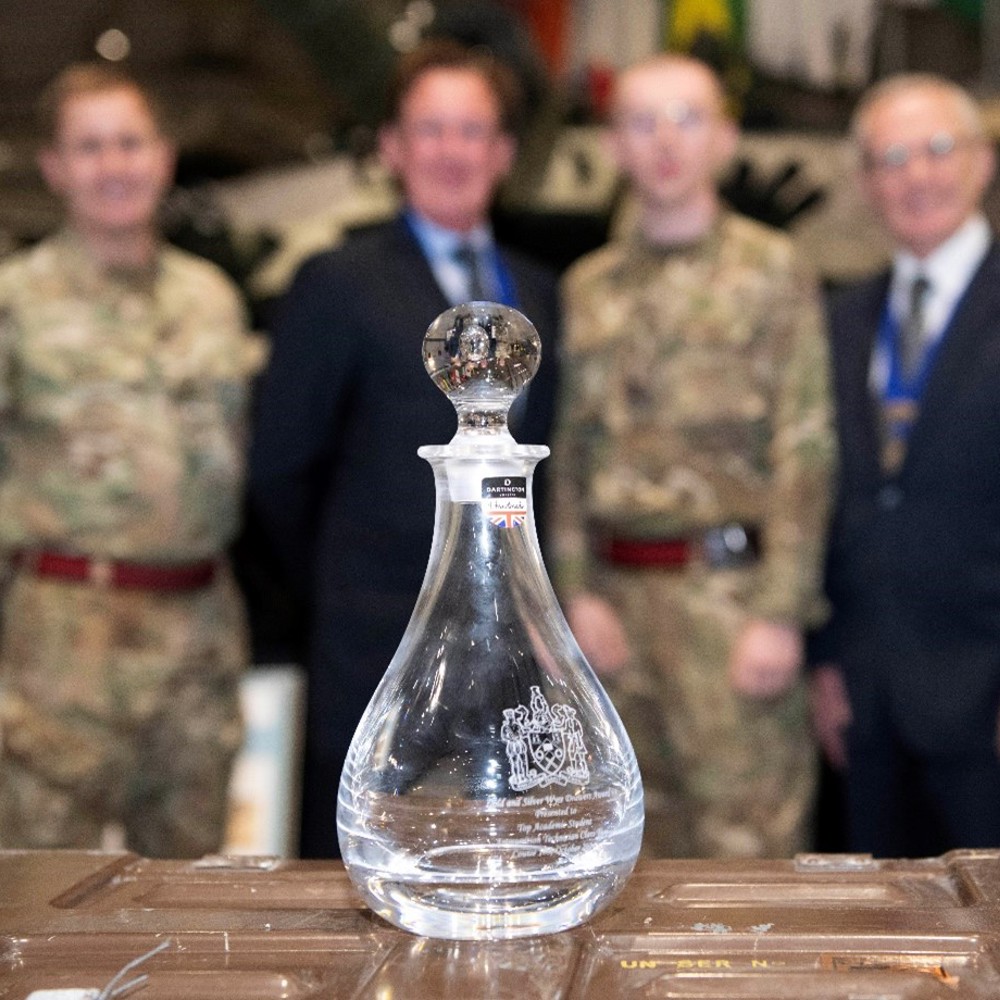 A cut glass decanter resting on a trunk in the foreground while the winner and presenters are in the background, blurred