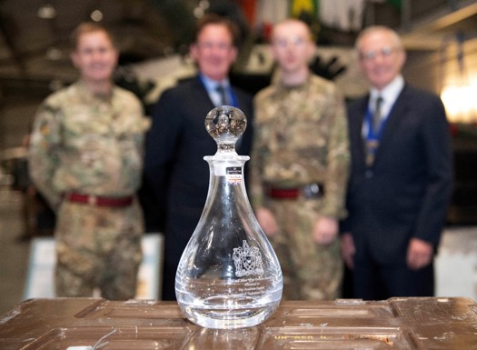 A cut glass decanter resting on a trunk in the foreground while the winner and presenters are in the background, blurred