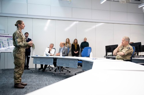 Military sat around a u-shape configured desk inside a classroom being presented to.