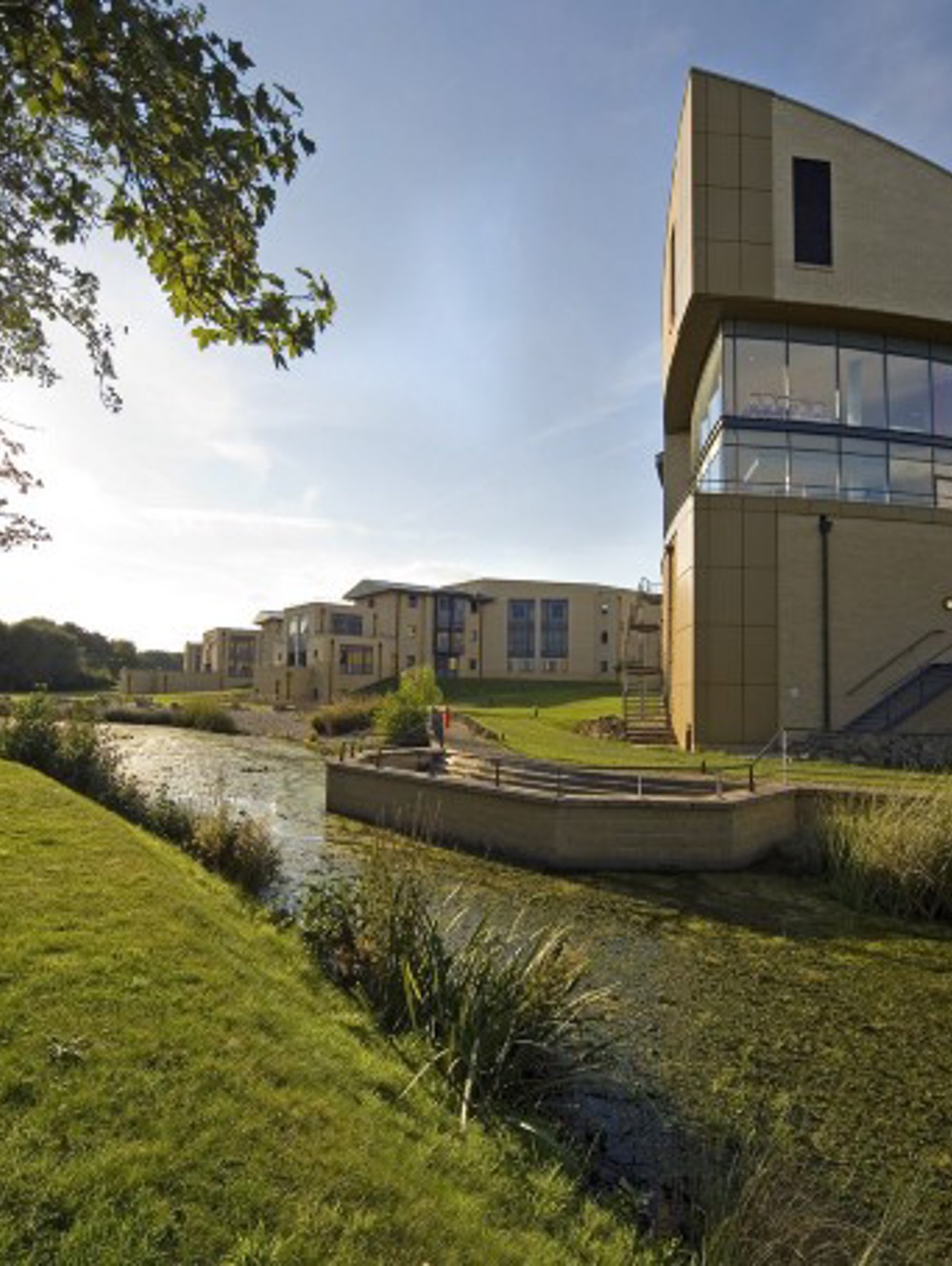 A ship-shaped wing of a building with a lake in the foreground and the sun setting behind.