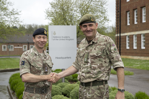 Two army officers shaking hands outside a building.