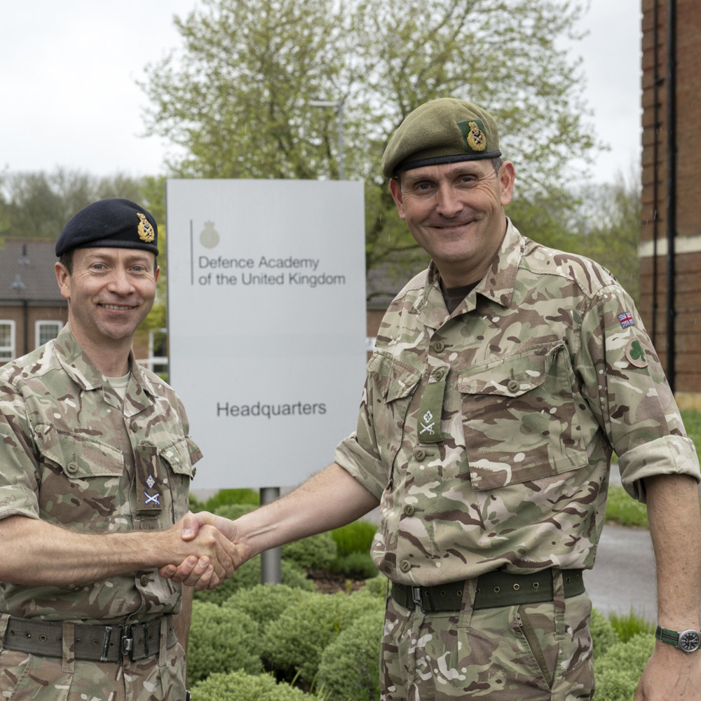 Two army officers shaking hands outside a building.