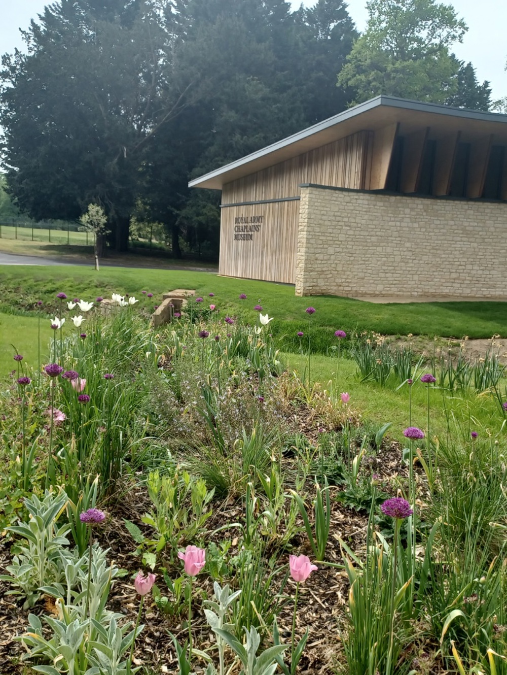 A new modern designed building with pink and purple flowers in the foreground surrounded by greenery.