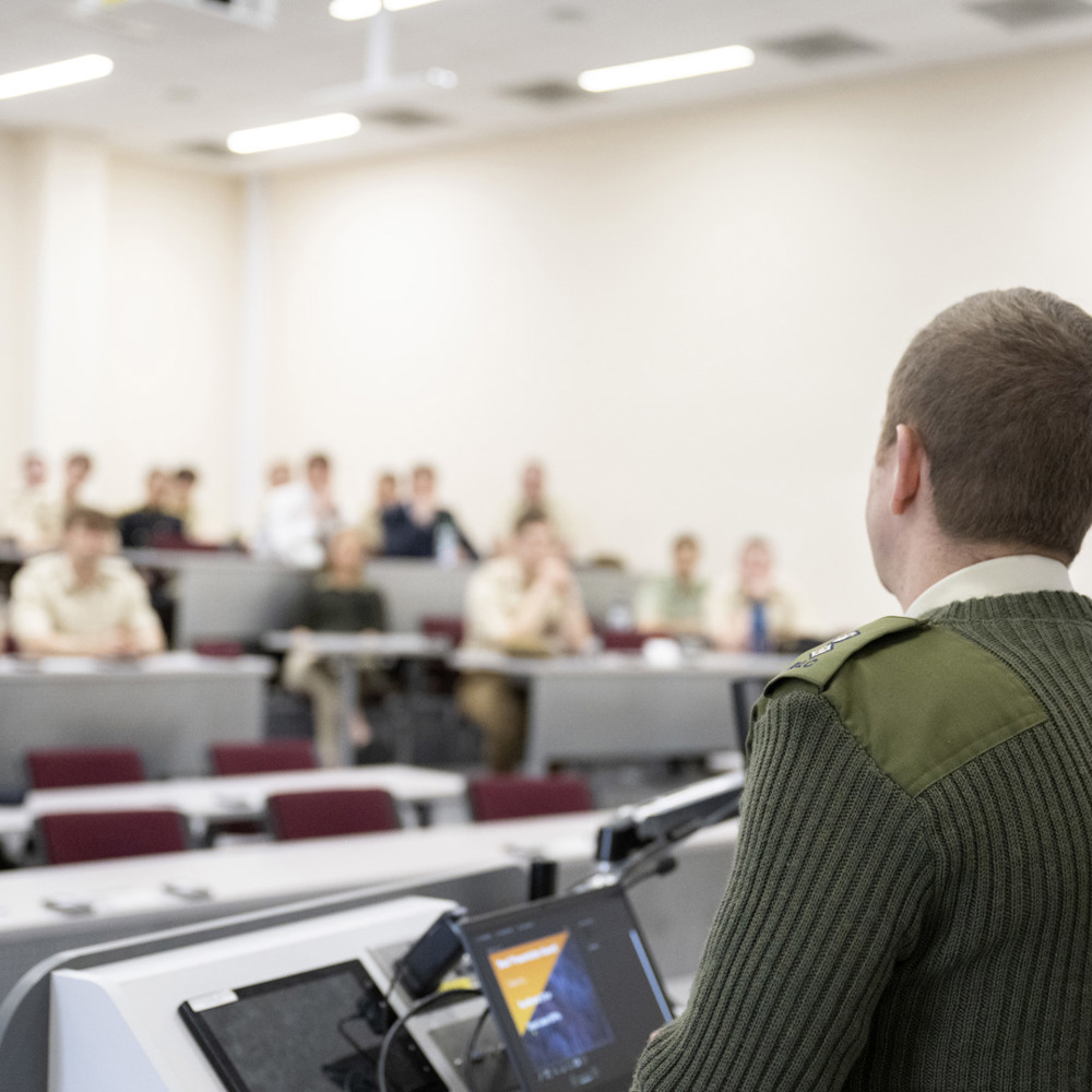 An army officer stood at a lectern presenting to an audience.