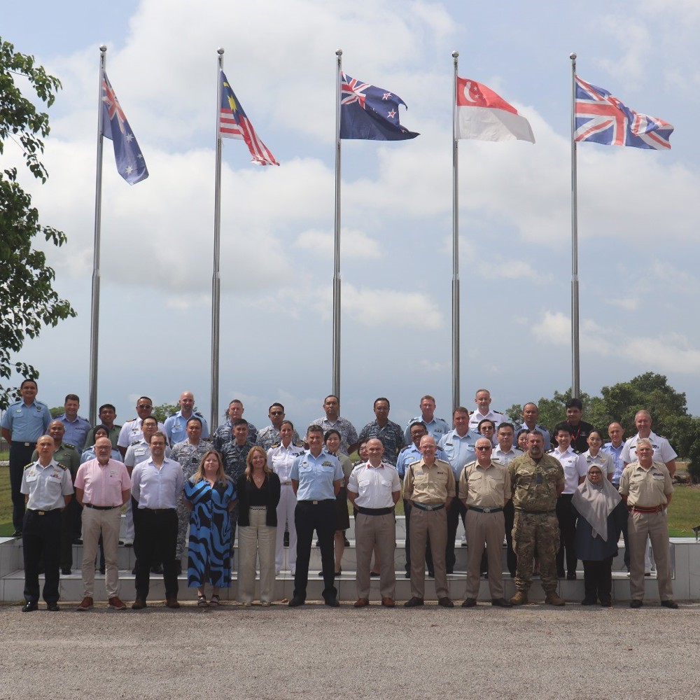 A group of military and civilian personnel stood in from of internal flags hung from posts outside. 