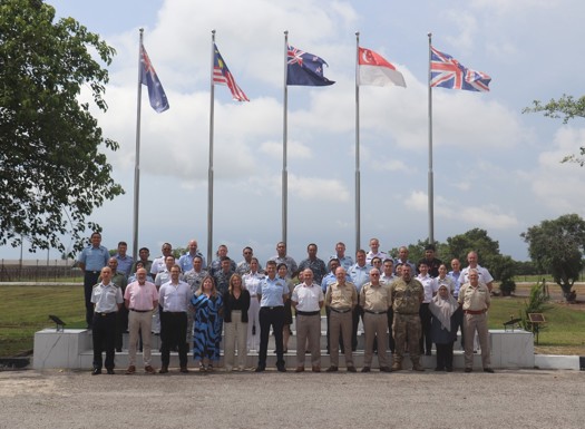 A group of military and civilian personnel stood in from of internal flags hung from posts outside. 