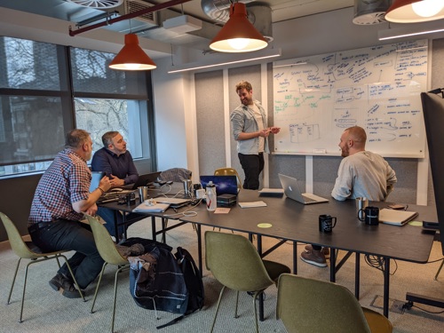 People gathered around desk and whiteboard brainstorming.