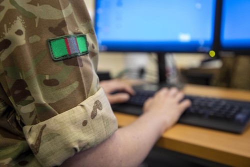 A close-up showing an officer in army combats typing on a computer.