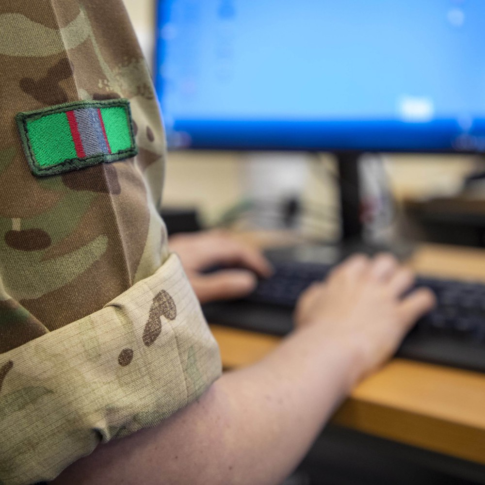 A close-up showing an officer in army combats typing on a computer.