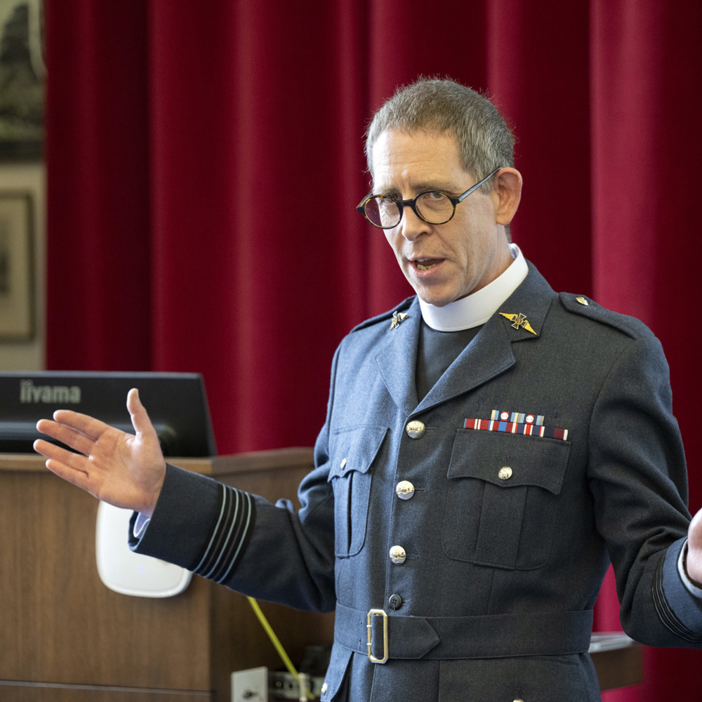 An RAF padre with his arms open addressing an unseen audience. 