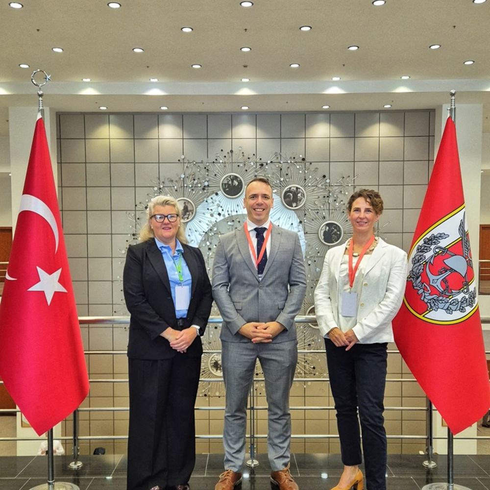 Three professionals stand between two Turkish flags in a modern lobby with a decorative wall installation behind them.