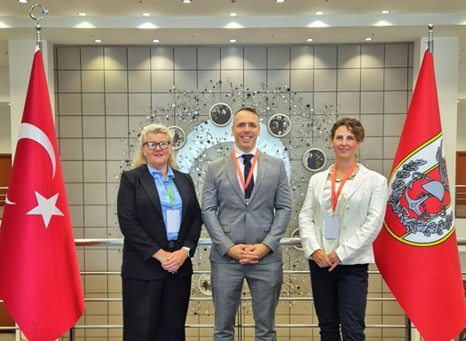 Three professionals stand between two Turkish flags in a modern lobby with a decorative wall installation behind them.
