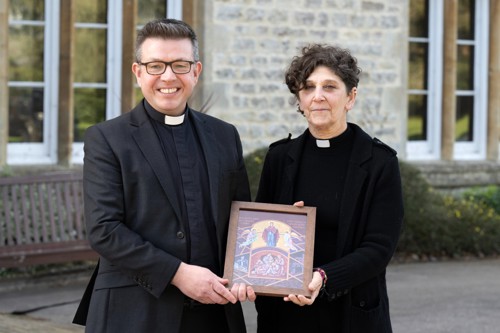 a female and Male Reverand holding a religious artwork.