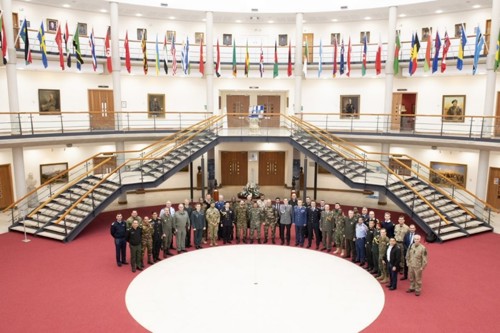 A group of personnel stood in a semi-circle surrounded by overhead international flags. 