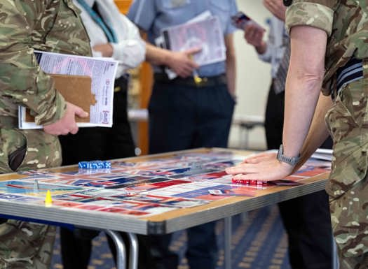 Tri-service personnel stood around a table playing a wargaming exercise. 