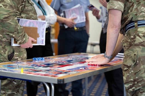 Tri-service personnel stood around a table playing a wargaming exercise. 
