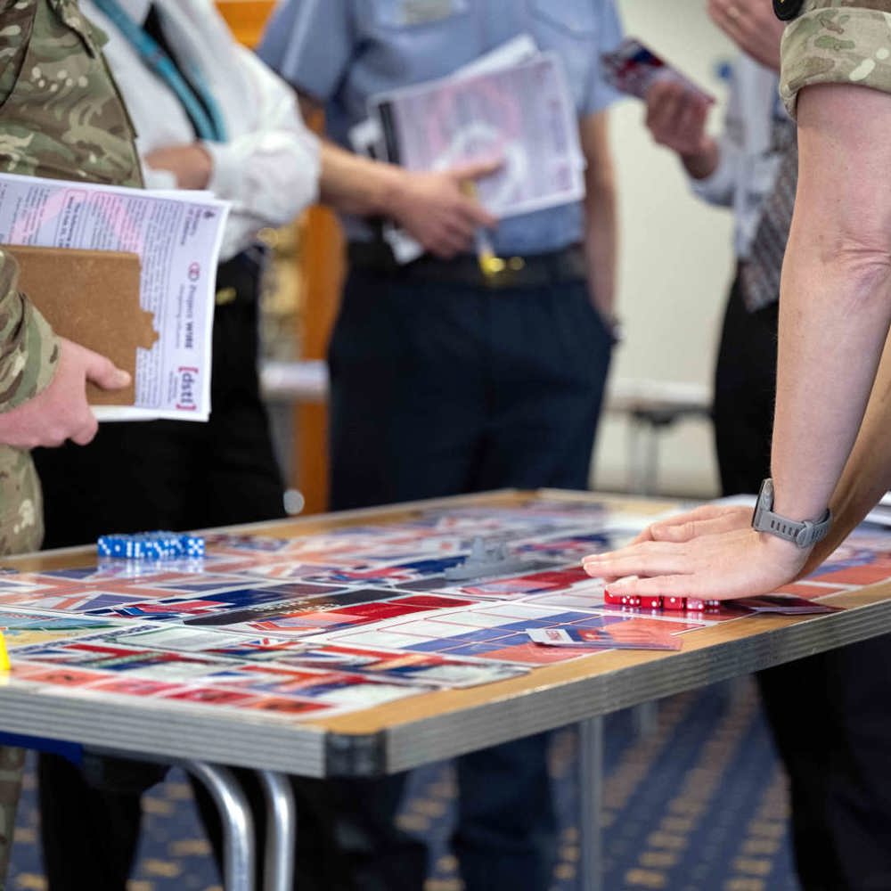 Tri-service personnel stood around a table playing a wargaming exercise.