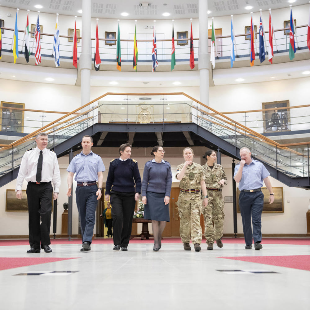 Tri-service personnel walking through the Forum with international flags hanging above them.
