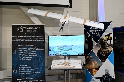 A white drone hanging above a TV screen with promotional banners either side.