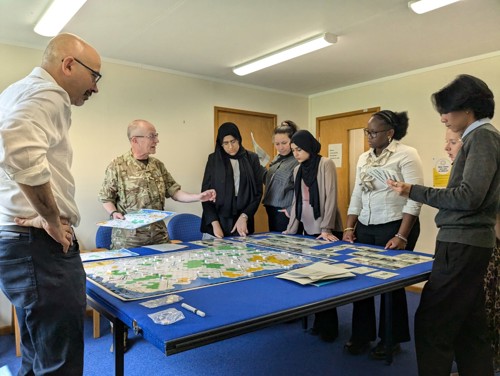 Students and MOD personnel in a classroom, wargaming around a table. 