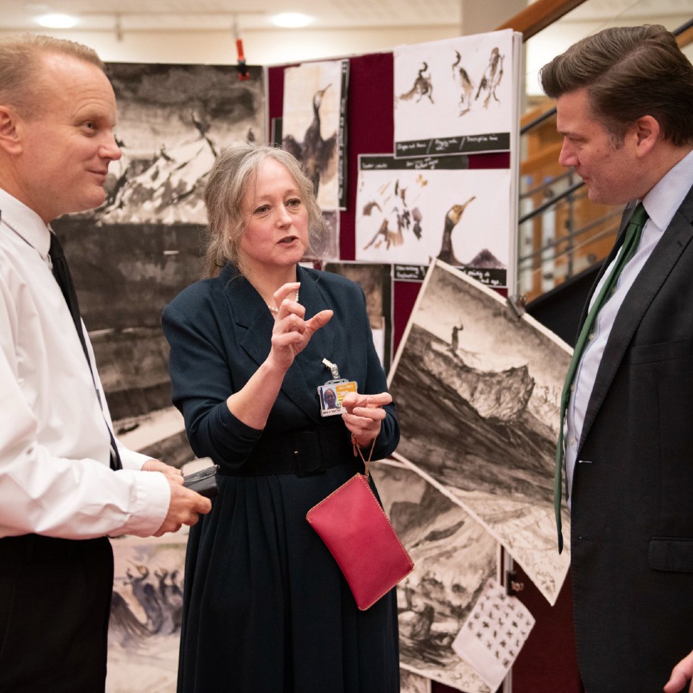 A navy officer, civilian and Minister for the Armed Forces talking with artwork in the background.