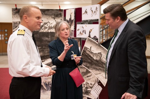 A navy officer, civilian and Minister for the Armed Forces talking with artwork in the background.