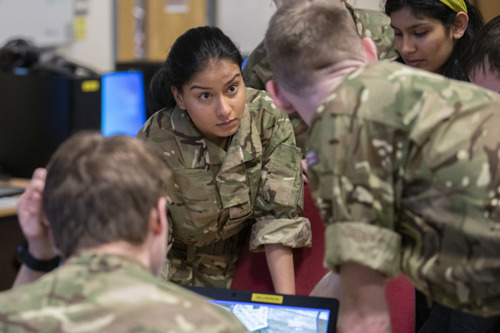 Young military student leaning over desk collaborating with peers.